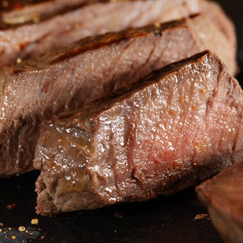 Fried cooked grilled meat with spices cut in slices served on dark slate. Closeup